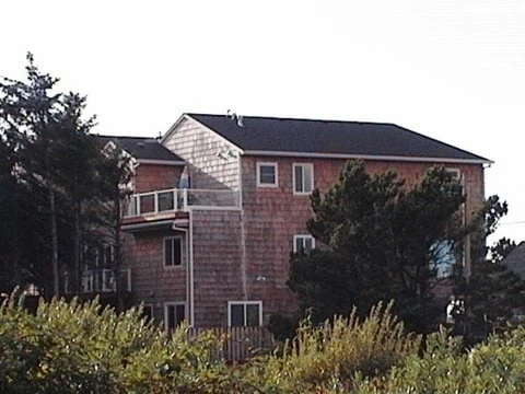 Cedar-shingle back of Sunset Cove 5 Bedroom in Seaside, with stacked decks among evergreens.